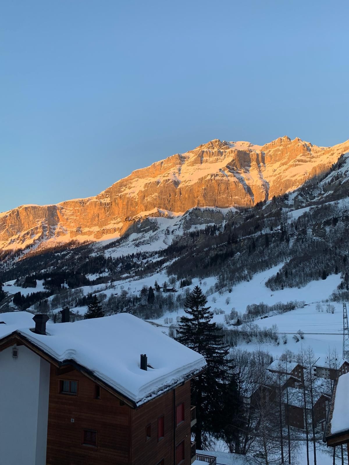 Evening alpenglow on the cliffs above Leukerbad, seen over snowy chalet roofs