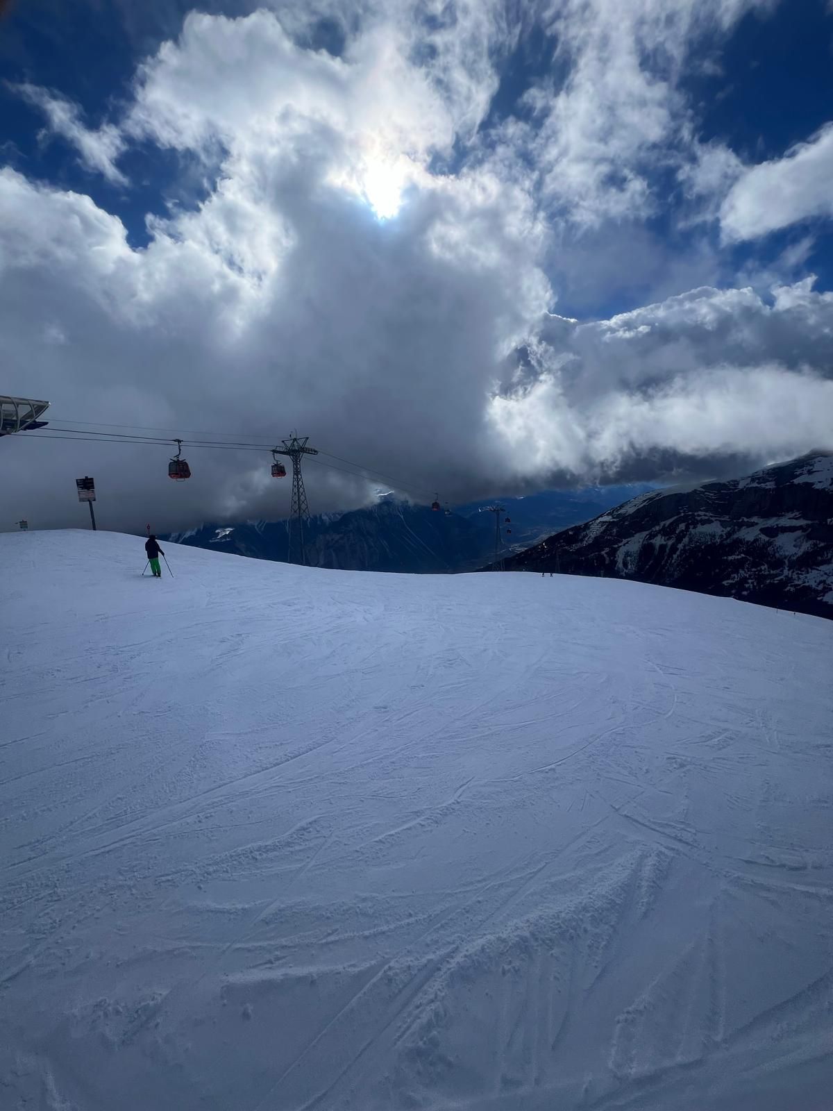 Skier on a wide piste below red gondolas