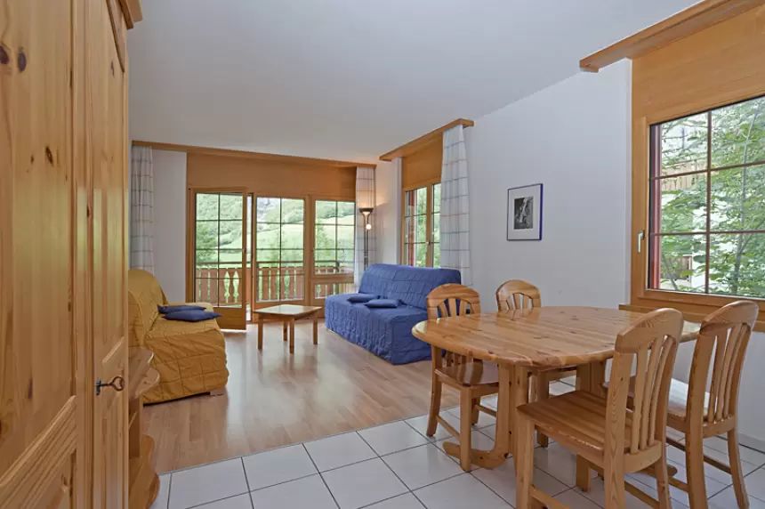 Living and dining room with pine table, blue and yellow sofas, and balcony doors