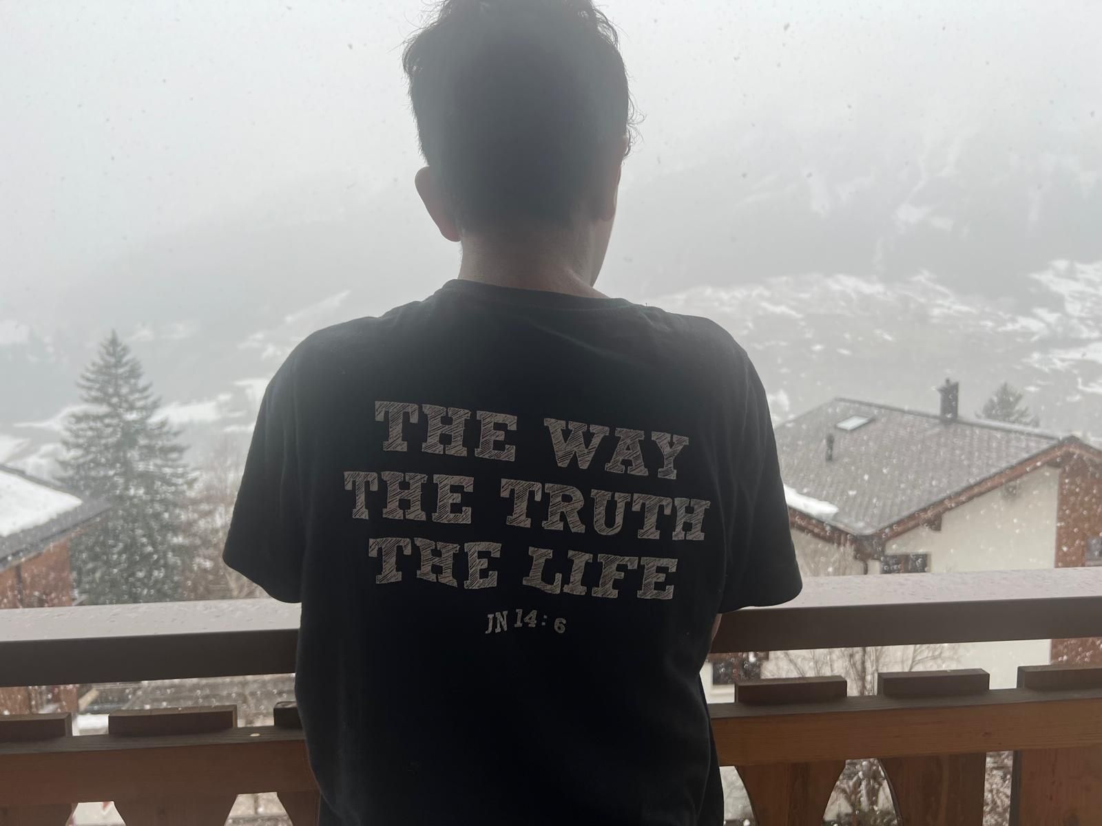A guest on the snowy balcony wearing a shirt that reads The Way, The Truth, The Life